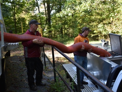 Hatchery personnel transferring trout from truck to truck with stocking hose
