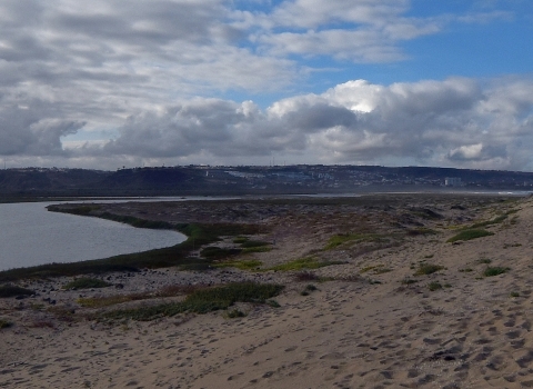 A river coming from the left curves to meet the ocean with a sandy beach in the foreground