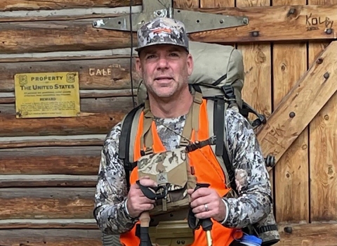 man in camo, orange vest holding hiking poles
